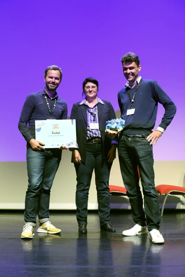 Trois personnes posent sur scène avec un trophée et un diplôme Treebal lors de la 18e édition des Trophées bretons des transitions, devant un fond violet.