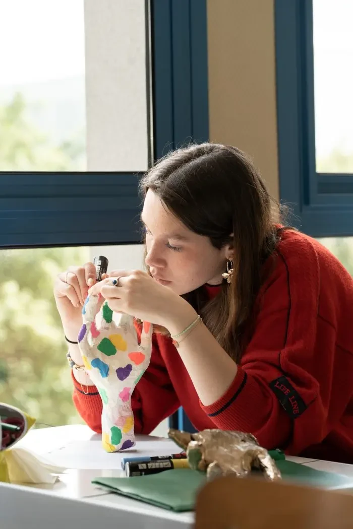 Jeune femme en pleine peinture sur une sculpture colorée représentant une main, dans un cadre lumineux
