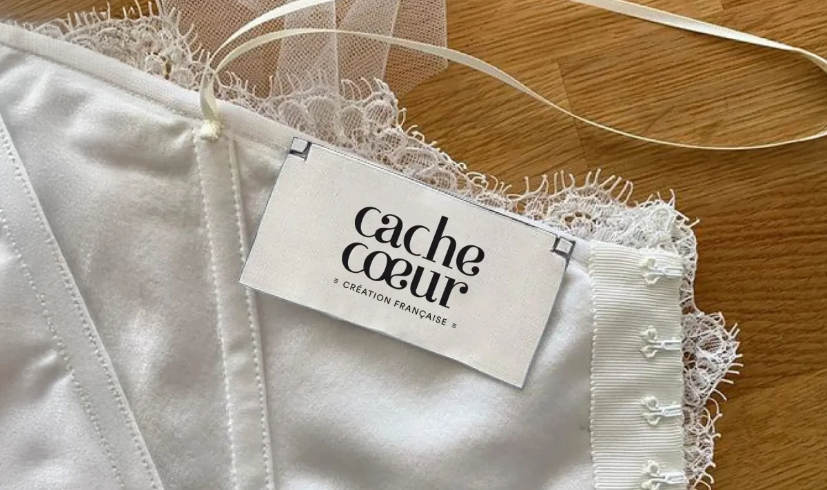 Étiquette de la marque Cache Cœur attachée à un soutien-gorge en dentelle blanche, symbole d’élégance et de douceur