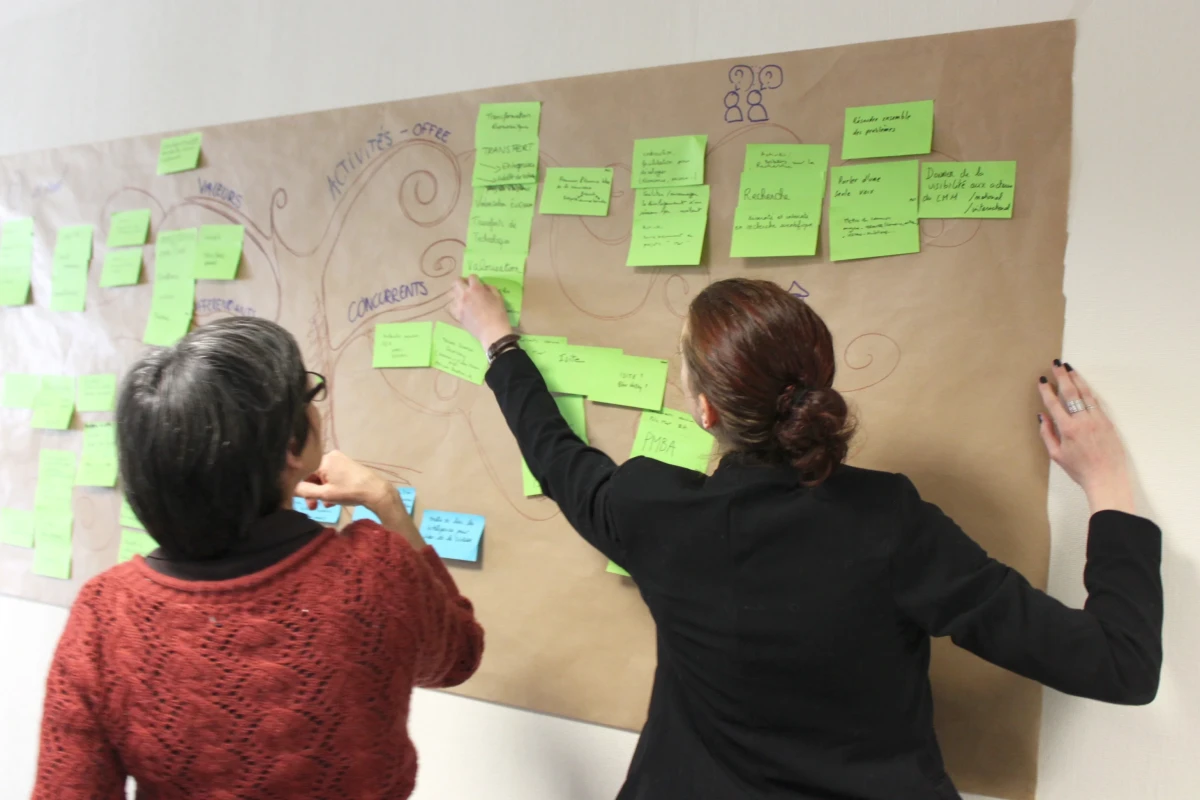 Deux participantes échangent lors d’un atelier de réflexion du Campus mondial de la mer, ajoutant des post-it sur un support collectif illustrant la démarche participative et l’intelligence territoriale autour de l’économie maritime durable.