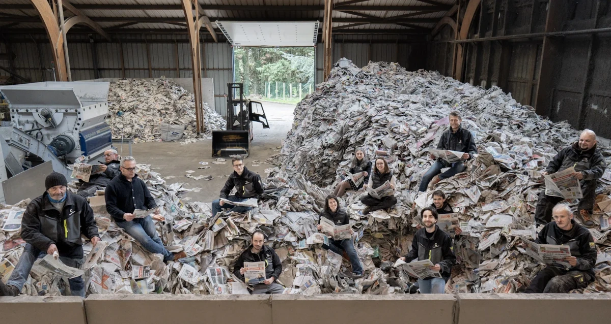 Photo d’équipe de Cellaouate dans un entrepôt rempli de journaux destinés au recyclage, illustrant l’engagement collectif de l’entreprise dans l’économie circulaire et la production d’isolants biosourcés.