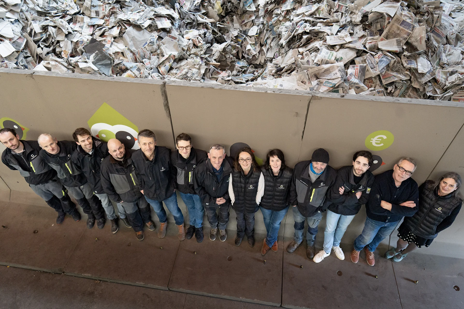 Vue de haut de l’équipe Cellaouate alignée devant un mur décoré de symboles de l’entreprise, soulignant la cohésion et la fierté collective autour du projet industriel local et durable.