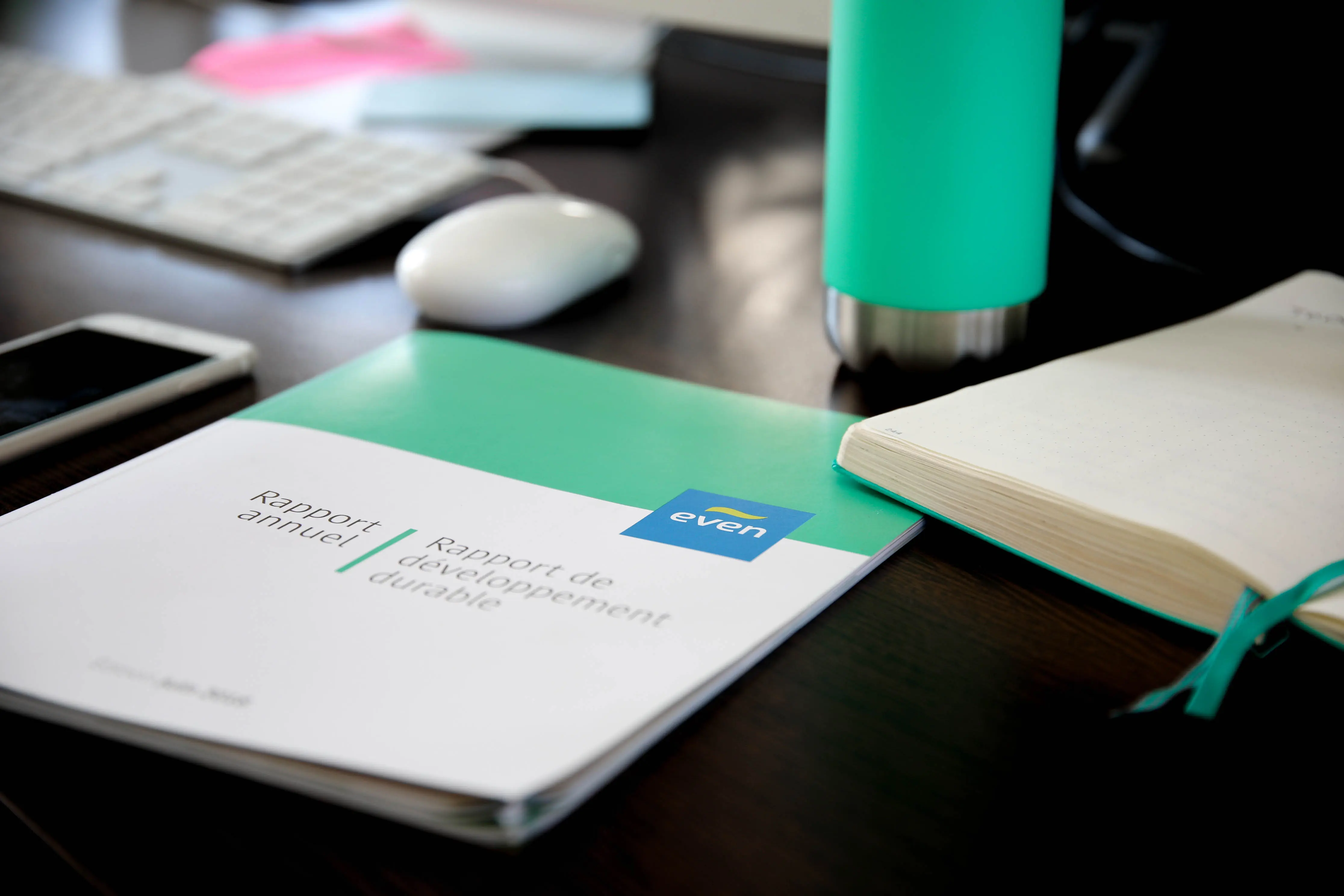 Rapport annuel Even 2022 posé sur un bureau, accompagné d’un carnet et d’une gourde couleur menthe