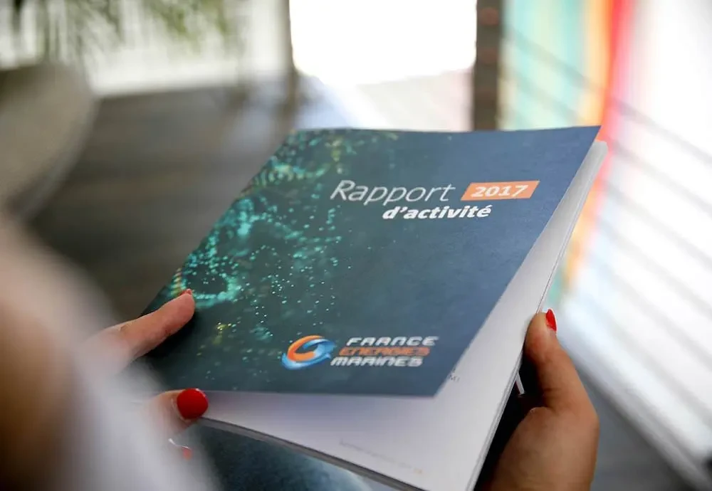 Main tenant le rapport d’activité 2017 de France Énergies Marines, incarnant l’engagement pour les énergies marines renouvelables – conception éditoriale par Hippocampe
