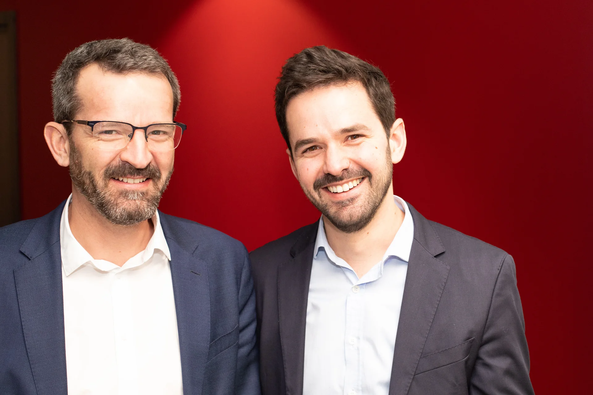 Portrait d'Antoine et François Bellion souriants devant un fond rouge, incarnant la continuité familiale et la dynamique entrepreneuriale au sein de la famille Bellion.