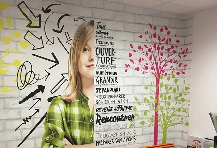 Fresque murale dans un hall d’établissement scolaire avec visuel d’élève, flèches graphiques et mots-clés pédagogiques