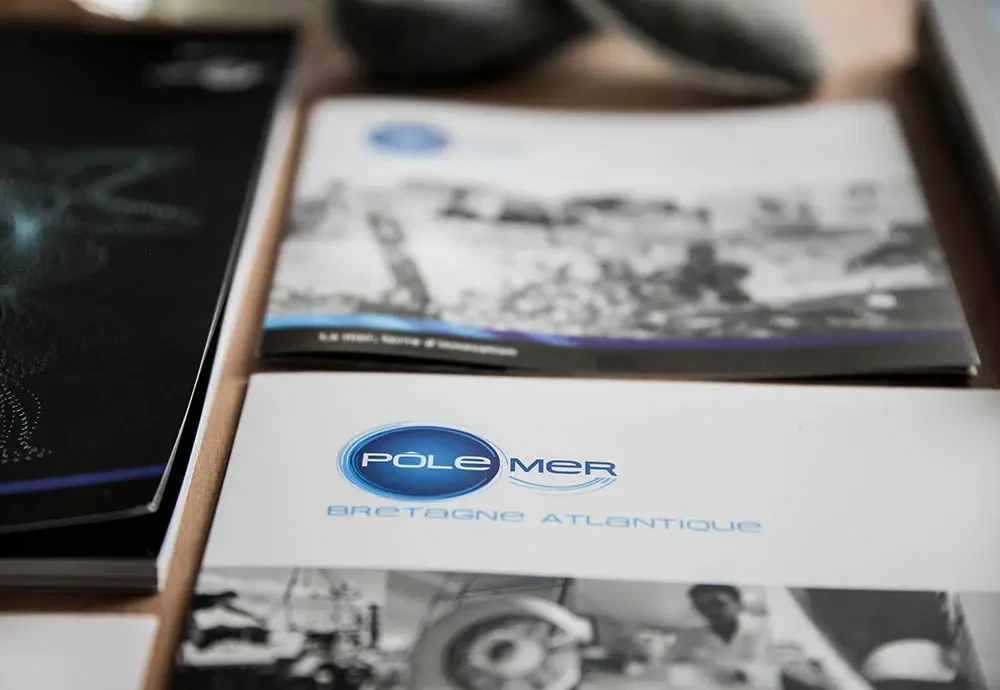 Ensemble de documents imprimés avec le logo bleu du Pôle Mer Bretagne Atlantique en couverture, posés sur une table en bois.