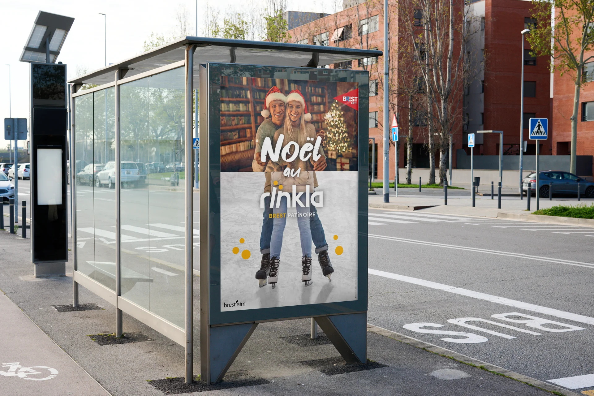 Affiche publicitaire Noël au Rïnkla installée dans un abribus, montrant un couple souriant portant des bonnets de Noël et des patins à glace devant un sapin illuminé.