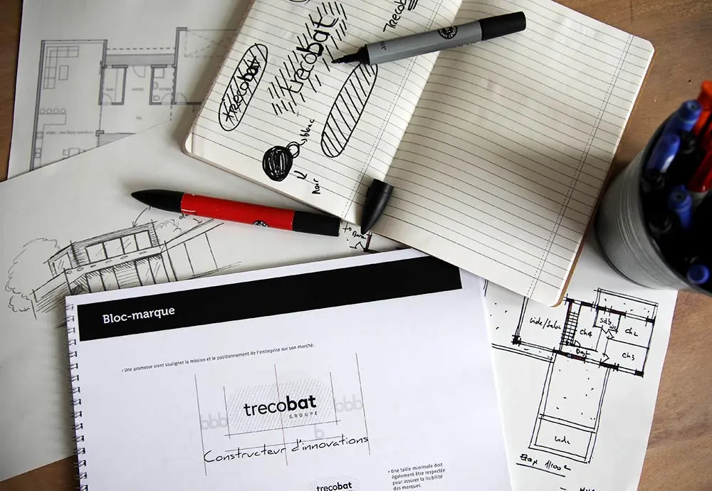 Page de définition du bloc-marque Trecobat entourée de croquis, d’un carnet de notes griffonné et de feutres