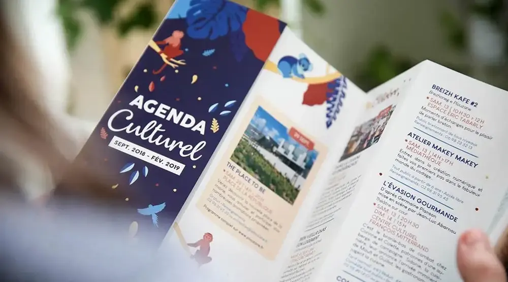 Habitante feuilletant l’agenda culturel illustré de Plouzané, imaginé par l’agence Hippocampe pour promouvoir les événements locaux entre septembre 2018 et février 2019