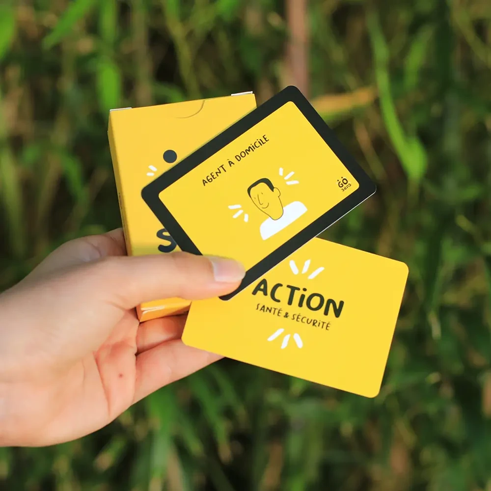 Une main tient un jeu de cartes illustrées aux couleurs vives, conçu par GoSens pour sensibiliser aux métiers de l’aide à domicile, avec une carte visible marquée « Agent à domicile ».